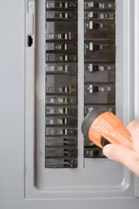 Hand holding an orange flashlight toward an electrical panel.