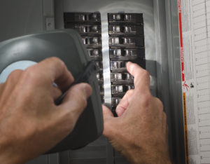 Hands at electrical panel, left hand holding a flashlight while the right hand flips a switch.