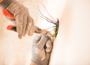 Electrician cutting wires from an access hole in a wall.