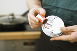 An individual carefully puts a battery inside a smoke detector, ensuring its readiness to detect smoke and prevent potential fires.