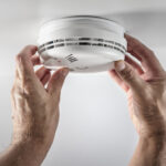 Hands reaching up to adjust their smoke alarm.