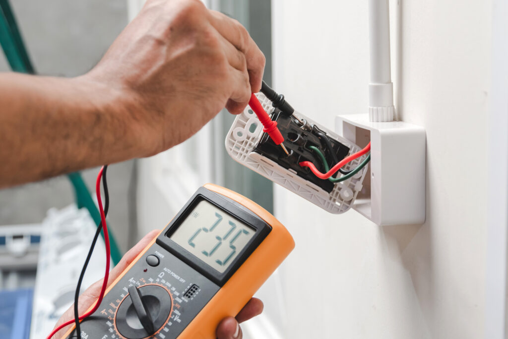 Electrician using a digital meter to measure the voltage at the power outlet in on the wall.