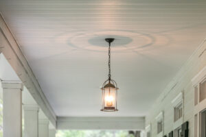 Hanging lantern on a front porch of a white house with a white ceiling and columns.